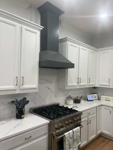 Detail of grey range hood, marble backsplash, and stainless gas range